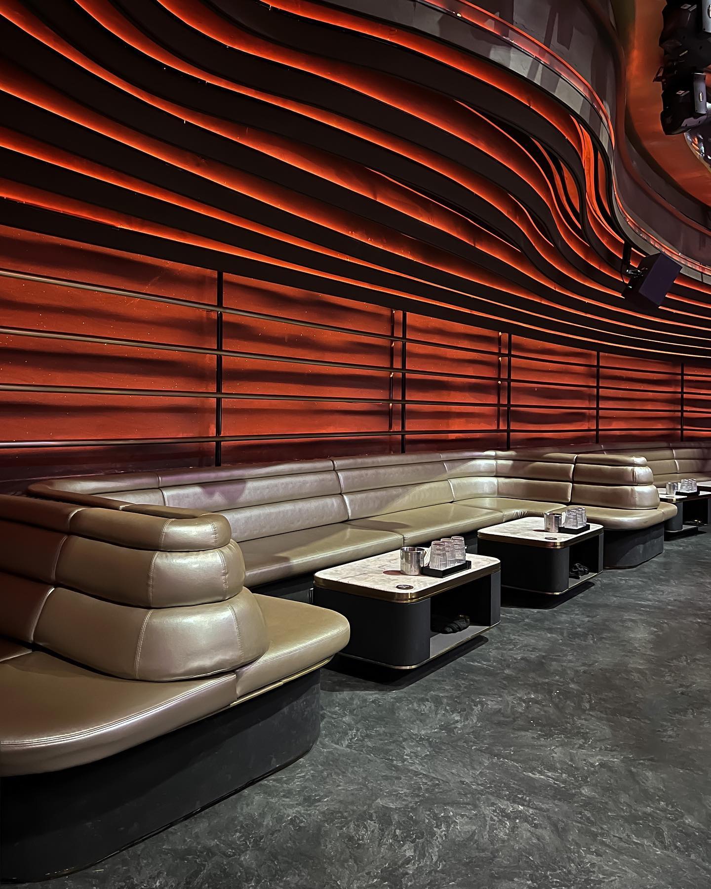 Curved tan leather booth with a wavy, illuminated red-orange wall background.