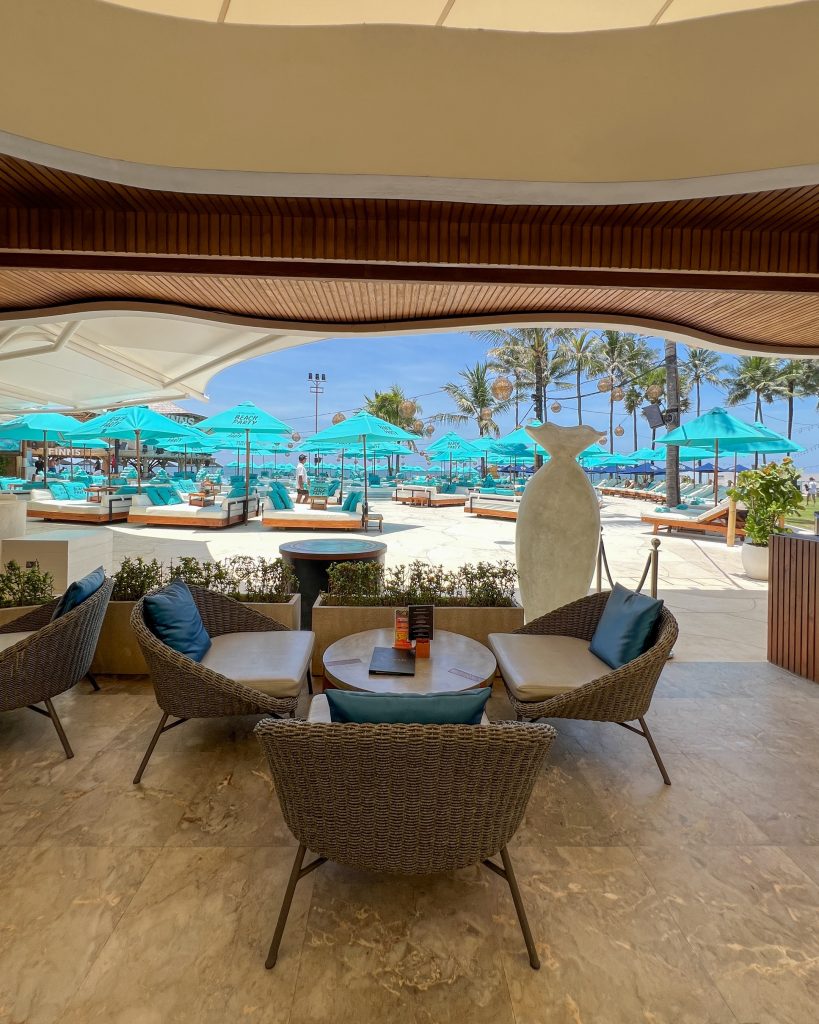 Open-air lounge seating overlooking Monsoon Bali at Finns VIP Beach Club, with turquoise umbrellas, palm trees, and beachfront daybeds.