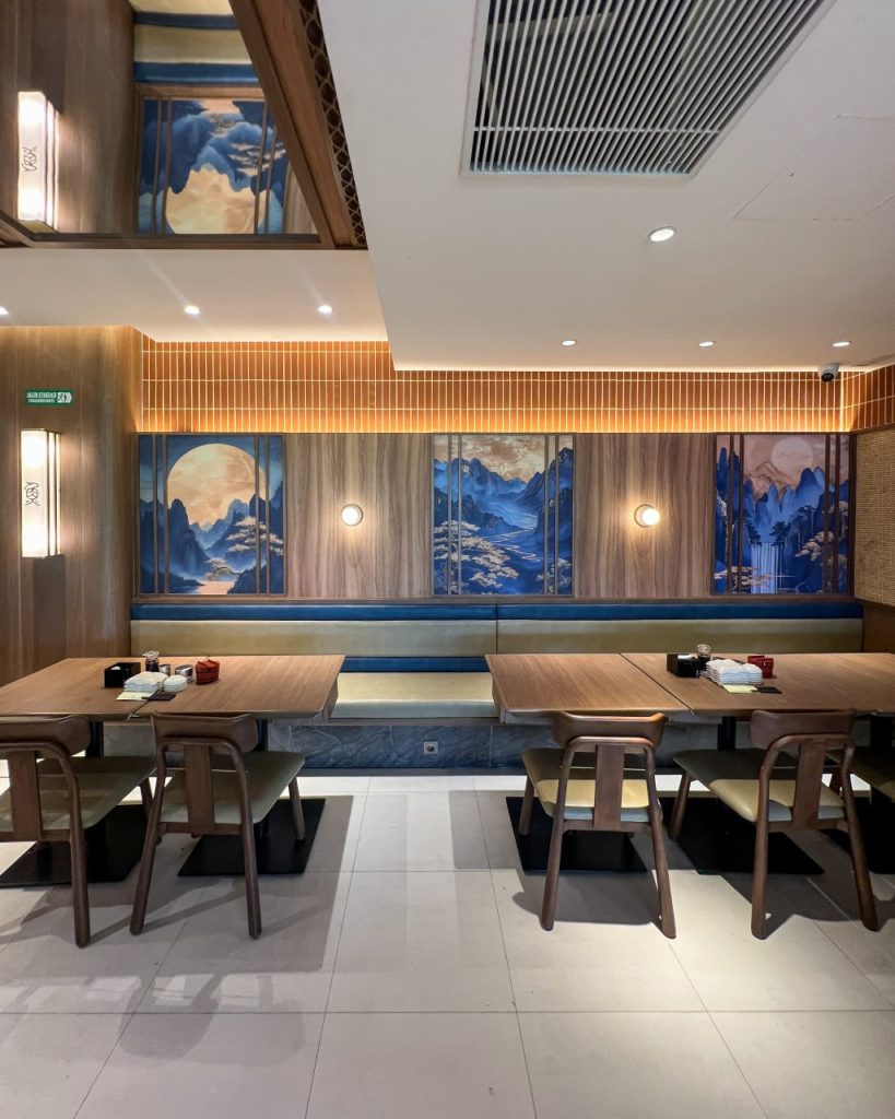 Modern dining area at Sushi Tei Beachwalk Bali with wooden tables, warm lighting, and blue-toned mural artwork along the walls.